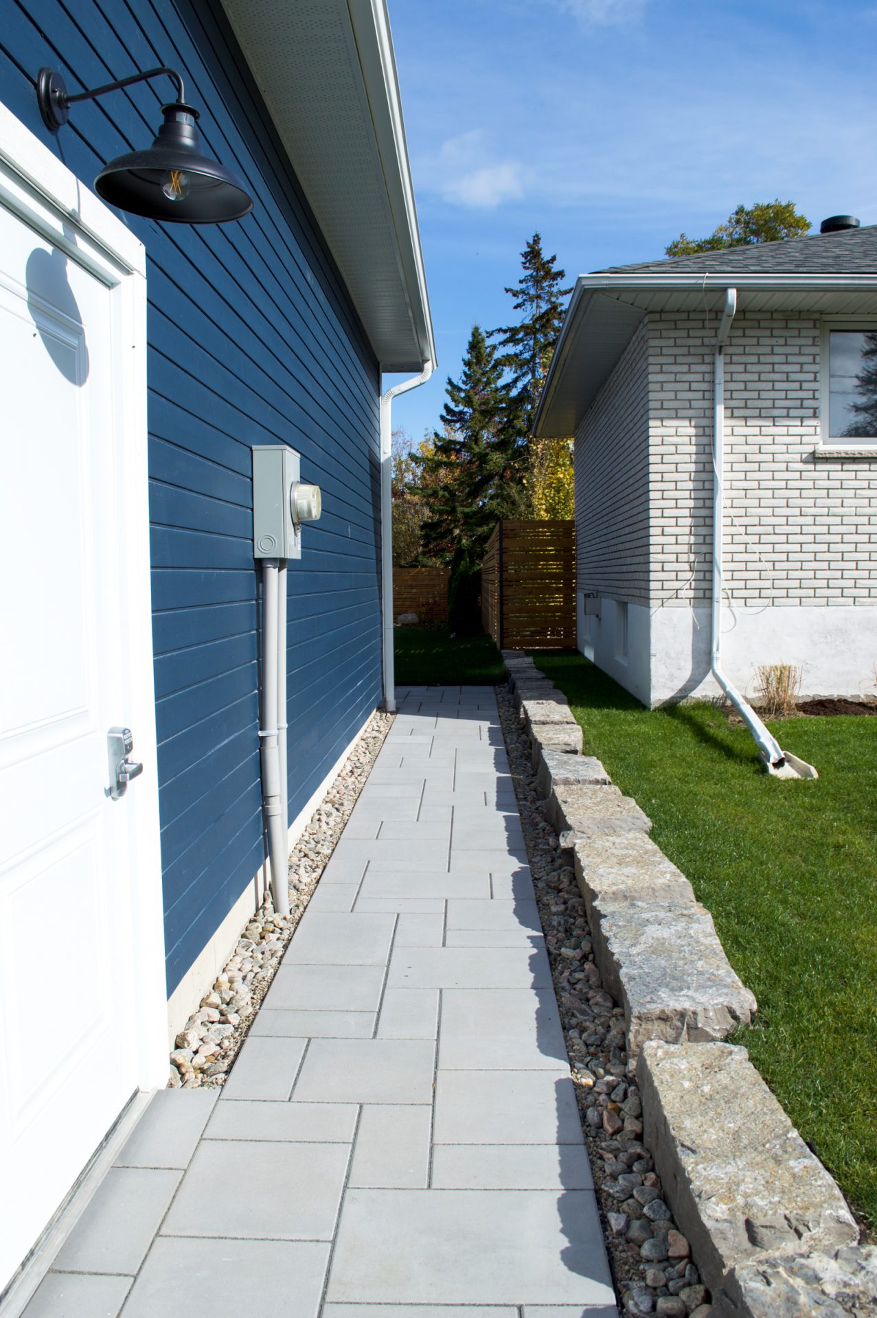 Narrow paved walkway beside blue house exterior