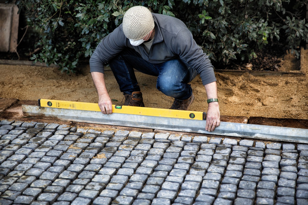 Worker leveling cobblestone pavers with spirit level