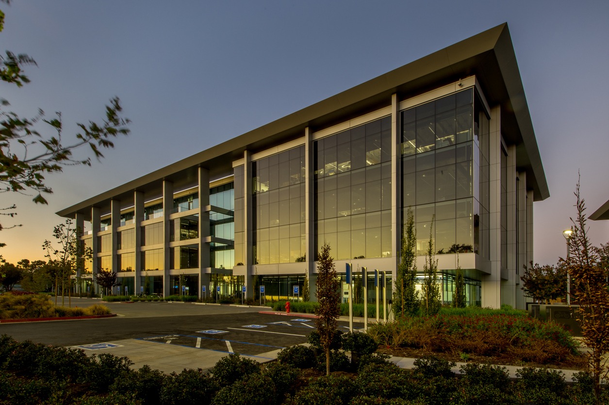 Modern glass office building at dusk with parking lot