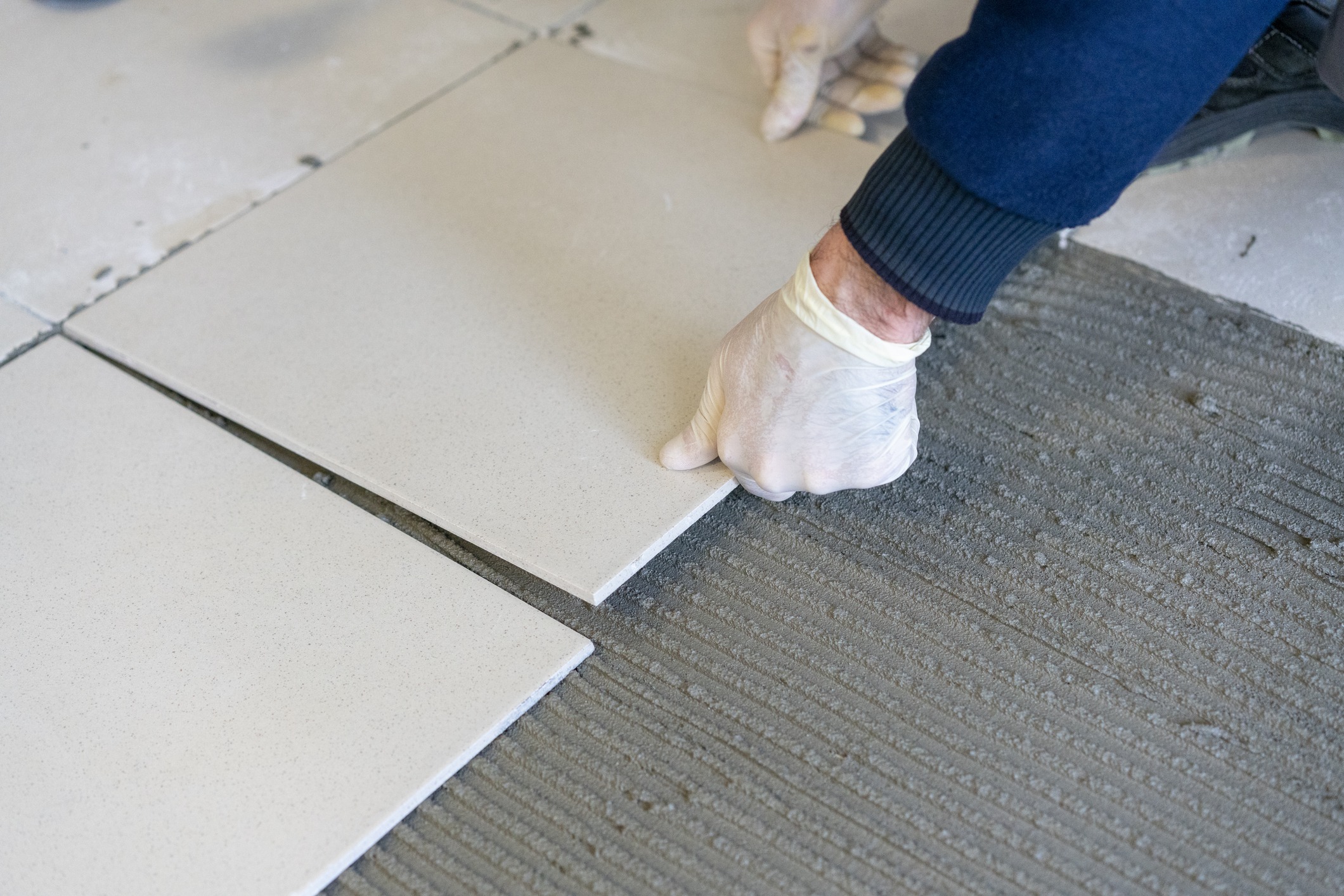 Gloved hand installing ceramic floor tile