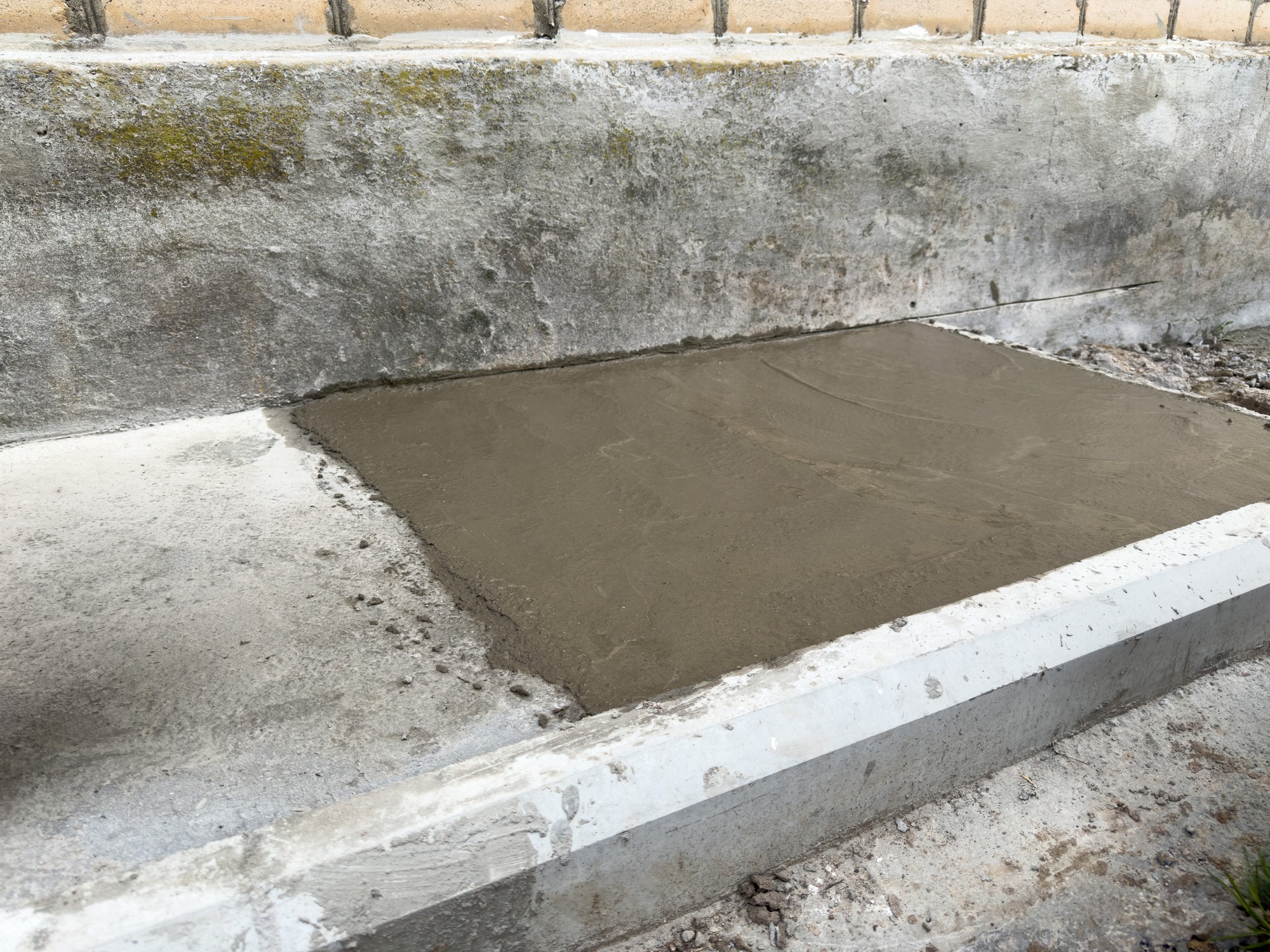Freshly poured concrete slab beside exterior wall